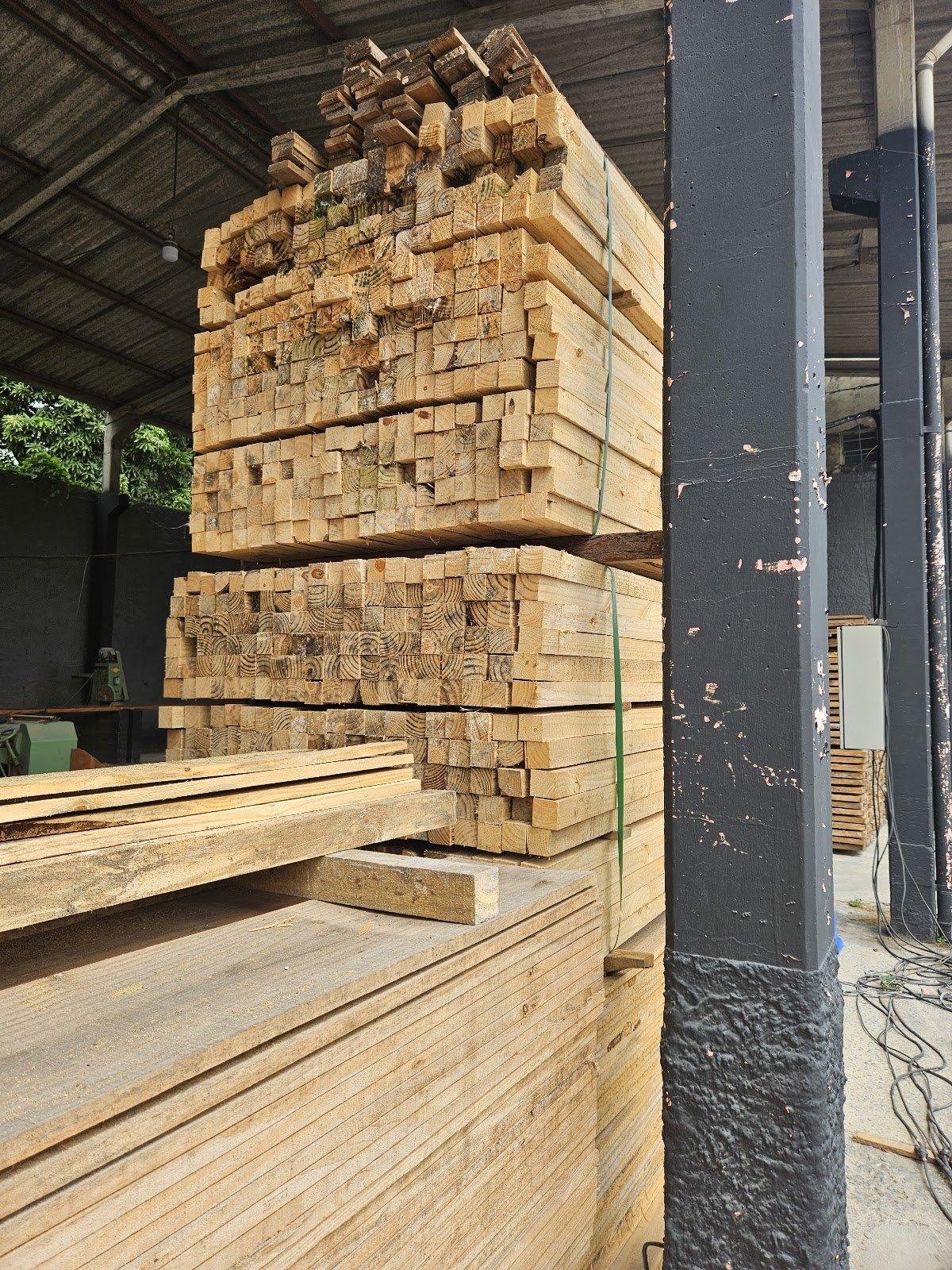 Pilha organizada de madeiras estruturais e tábuas em um ambiente de madeireira.