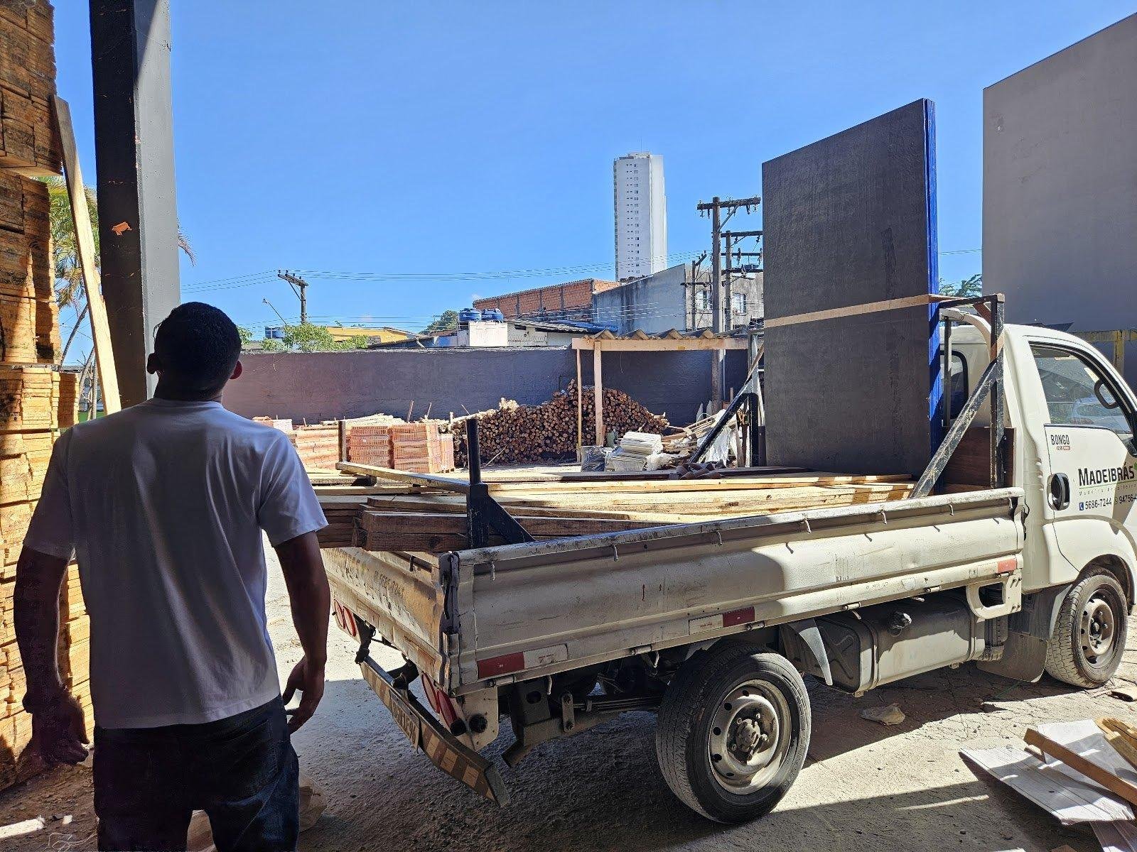 Um funcionário carregando um caminhão com chapas de madeira em um pátio de madeireira.