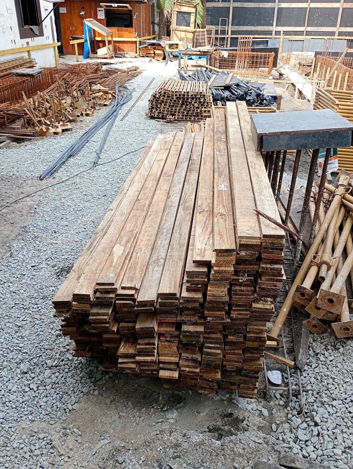 Pilha de madeira serrada (tábuas) em um canteiro de obras.