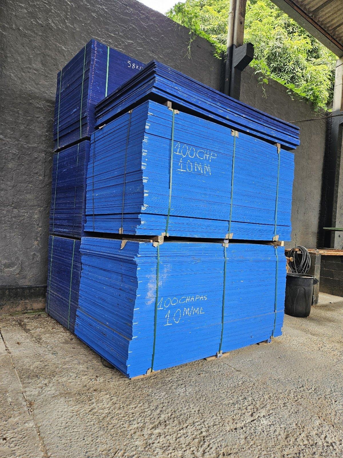 Pilhas de chapas de madeira azul organizadas no pátio.